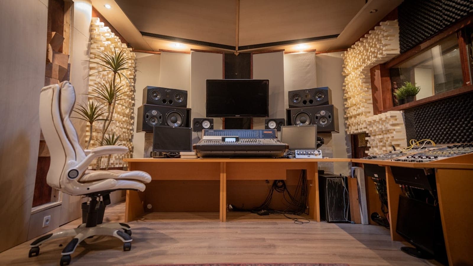 A recording control room — mixing desk, studio monitors either side of a screen, acoustic diffusers on the walls.
