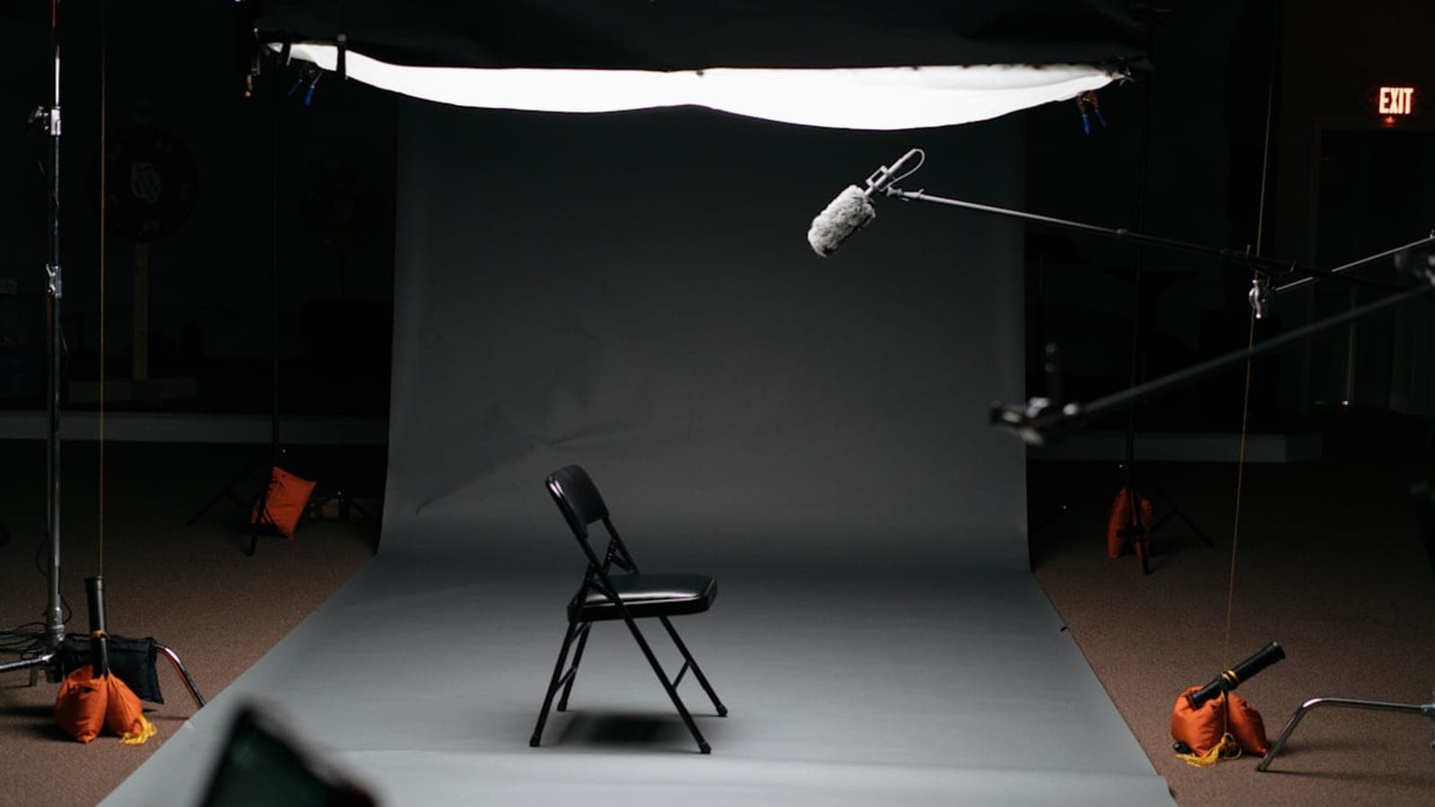 A video stage — grey backdrop, a single chair and a boom microphone under a diffused light.